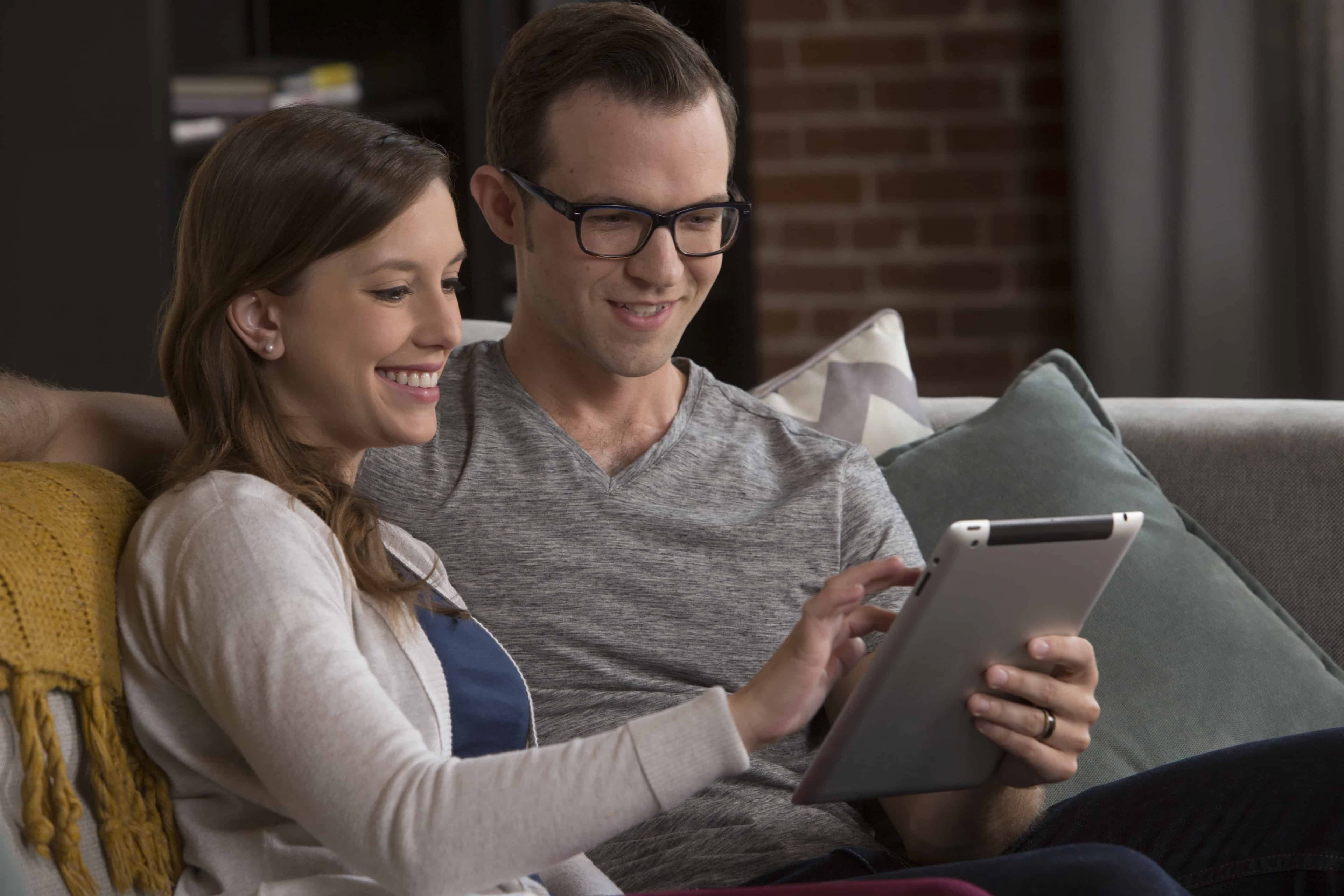 Couple sitting on their couch planning their move on a tablet - Mayflower®